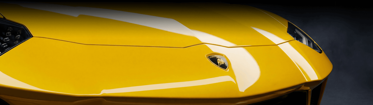 Close-up view of the front hood of a yellow Lamborghini sports car, showing its sharp lines, glossy finish, headlight details, and the Lamborghini emblem in the center.