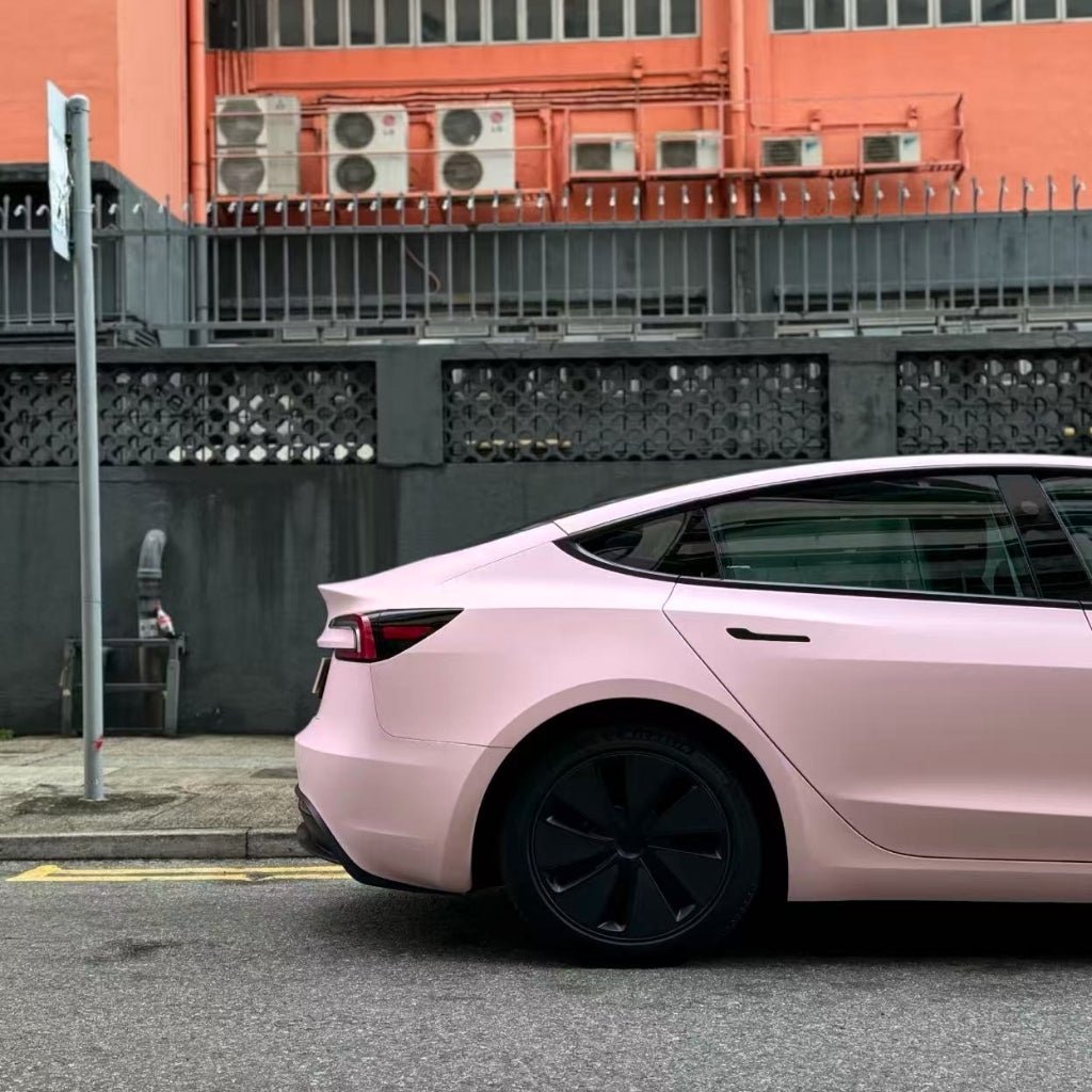 A Baby Pink SelfRepair Nano-Coated PPF car is parked by a black fence, near a peach building with several AC units, highlighting its ochrana proti škrabancom for lasting beauty.