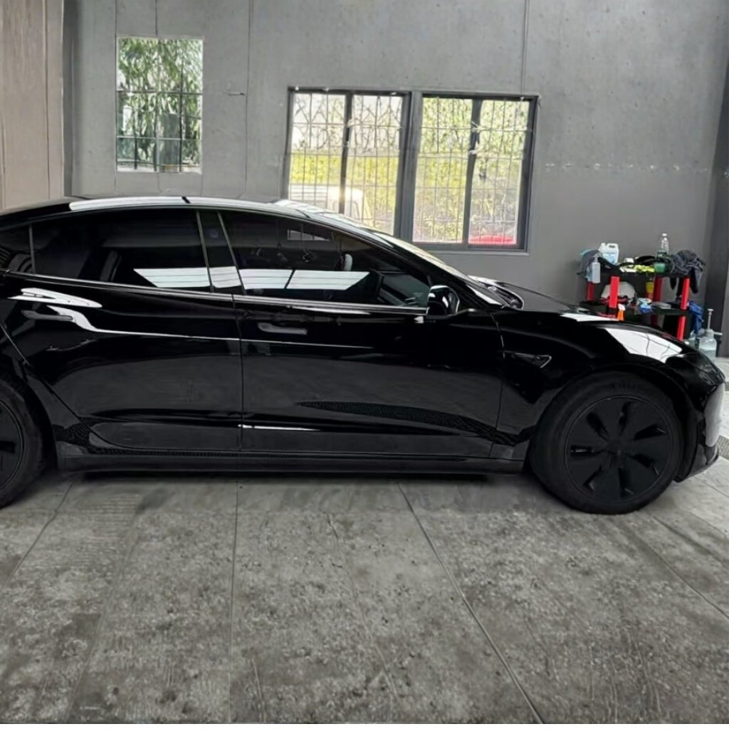 A car with a Black Glossy SelfRepair Nano-Coated PPF is parked indoors beside a wall with two windows. Nearby shelves and a cart hold cleaning supplies, emphasizing the workshop’s commitment to paint protection.