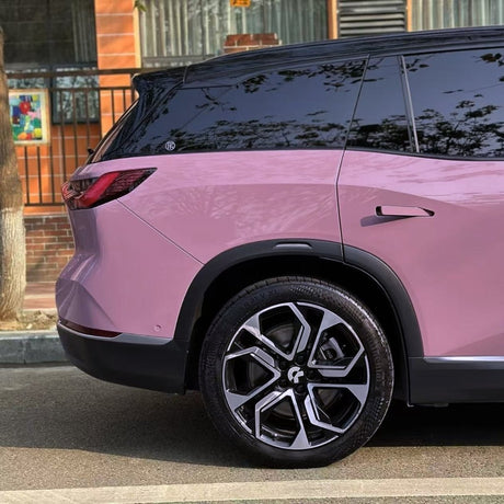 A close-up of the rear half of a pink SUV parked on a street shows Blush Mauve Glossy SelfRepair Nano-Coated PPF on the wheel, window, and taillight, with trees and a building in the background.