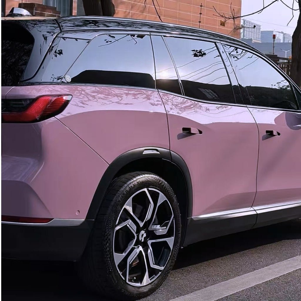 A sleek, modern SUV coated in Blush Mauve Glossy SelfRepair Nano-Coated PPF is parked by a brick building. It features tinted windows, black-and-silver alloy wheels, and a shiny finish reflecting sunlight on the city street.