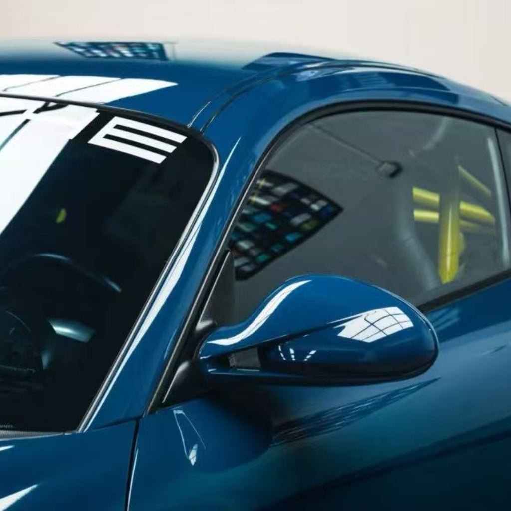 Close-up of a blue sports car’s side mirror and window, showing ceiling light reflections and colorful panels. The yellow seat belt is visible through the window, highlighting Deep Blue Glossy SelfRepair Nano-Coated PPF protection.