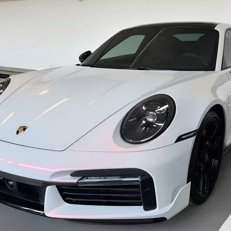A white Porsche sports car with black wheels is parked indoors in a well-lit showroom, viewed from the front left angle and protected by White Diamond Pink Glossy SelfRepair Nano-Coated PPF for a flawless finish.