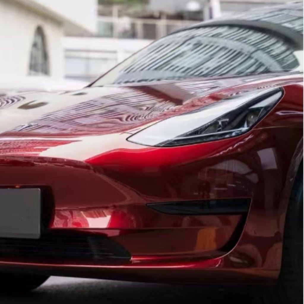 Close-up of the front left side of a shiny car with Dragon Blood Red Liquid Metallic Glossy SelfRepair Nano-Coated PPF, highlighting the sleek headlight, part of the hood, and reflections of modern architecture on its surface.
