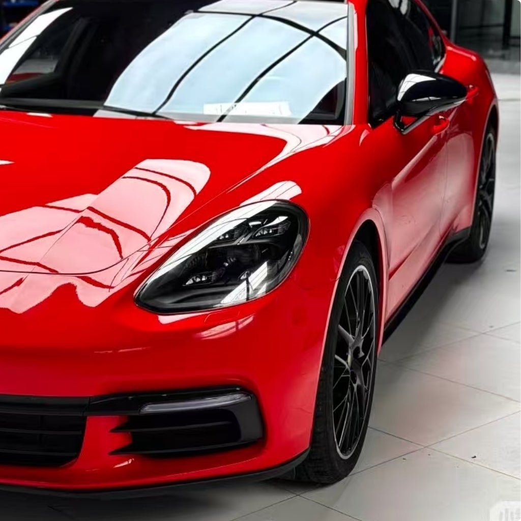 A shiny red sports car with Nexthor™ Ferrari Red SelfRepair Nano PPF Glossy is parked indoors on a tiled floor, reflecting ceiling lights and windows. The image shows the front and side, highlighting its sleek design and black alloy wheels.