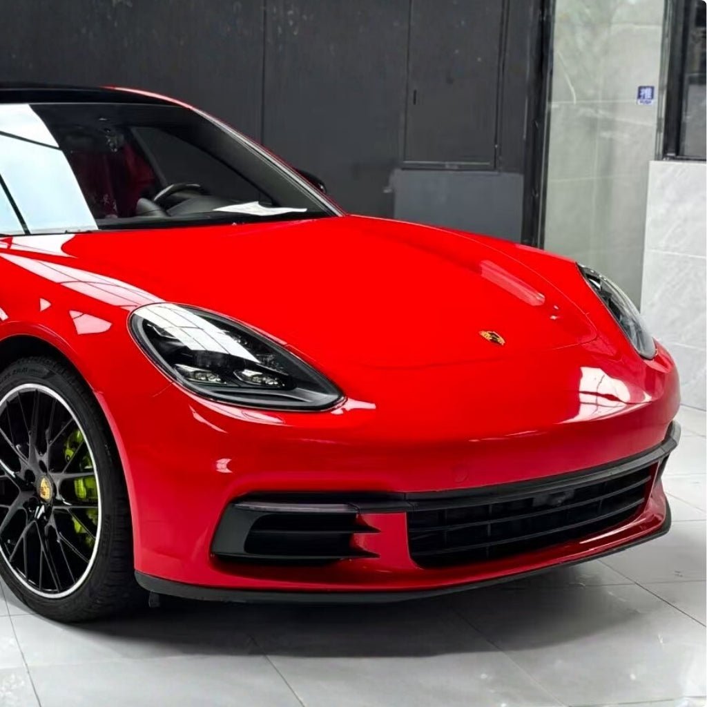 A shiny red Porsche with Nexthor™ Ferrari Red SelfRepair Nano PPF Glossy is parked indoors on a reflective white floor, displaying its front and left side, black rims, and sleek headlights.