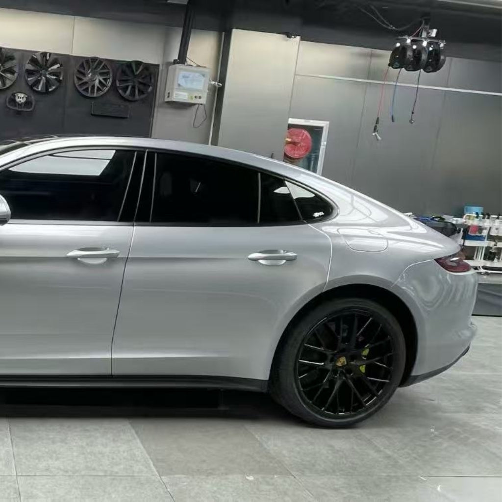 A luxury silver sedan with tinted windows and black alloy wheels is parked in a modern garage, showcasing its GT Silver Liquid Metallic Glossy SelfRepair Nano-Coated PPF. Gray walls, tools, and equipment are visible in the background.