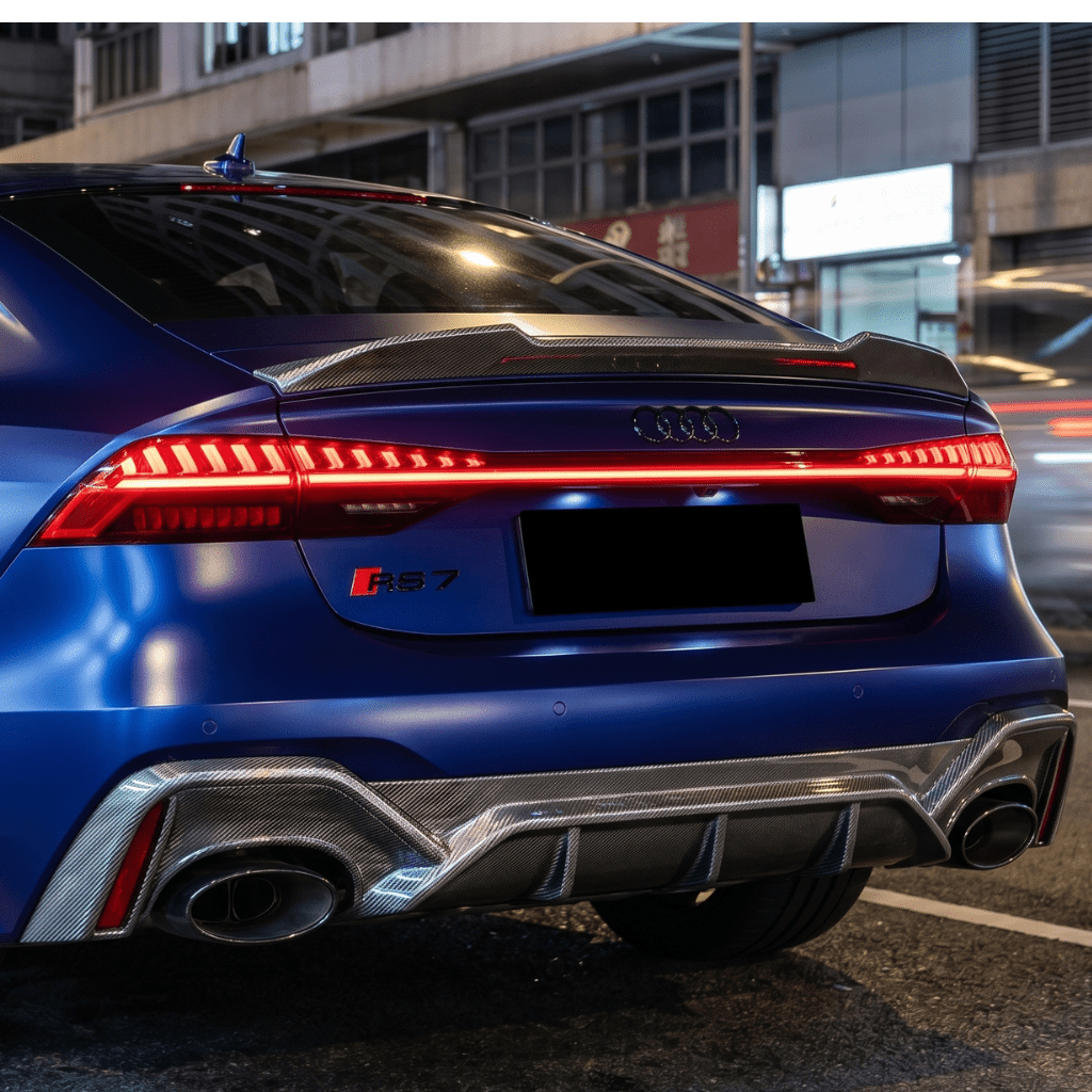 A close-up of the rear of a blue Audi RS7 features taillights, rear spoiler, dual exhausts, and RS7 badge, protected by Liquid Metallic Aluminium Carbon Fiber Self-Healing Nano-Coated PPF, parked on a city street at night.