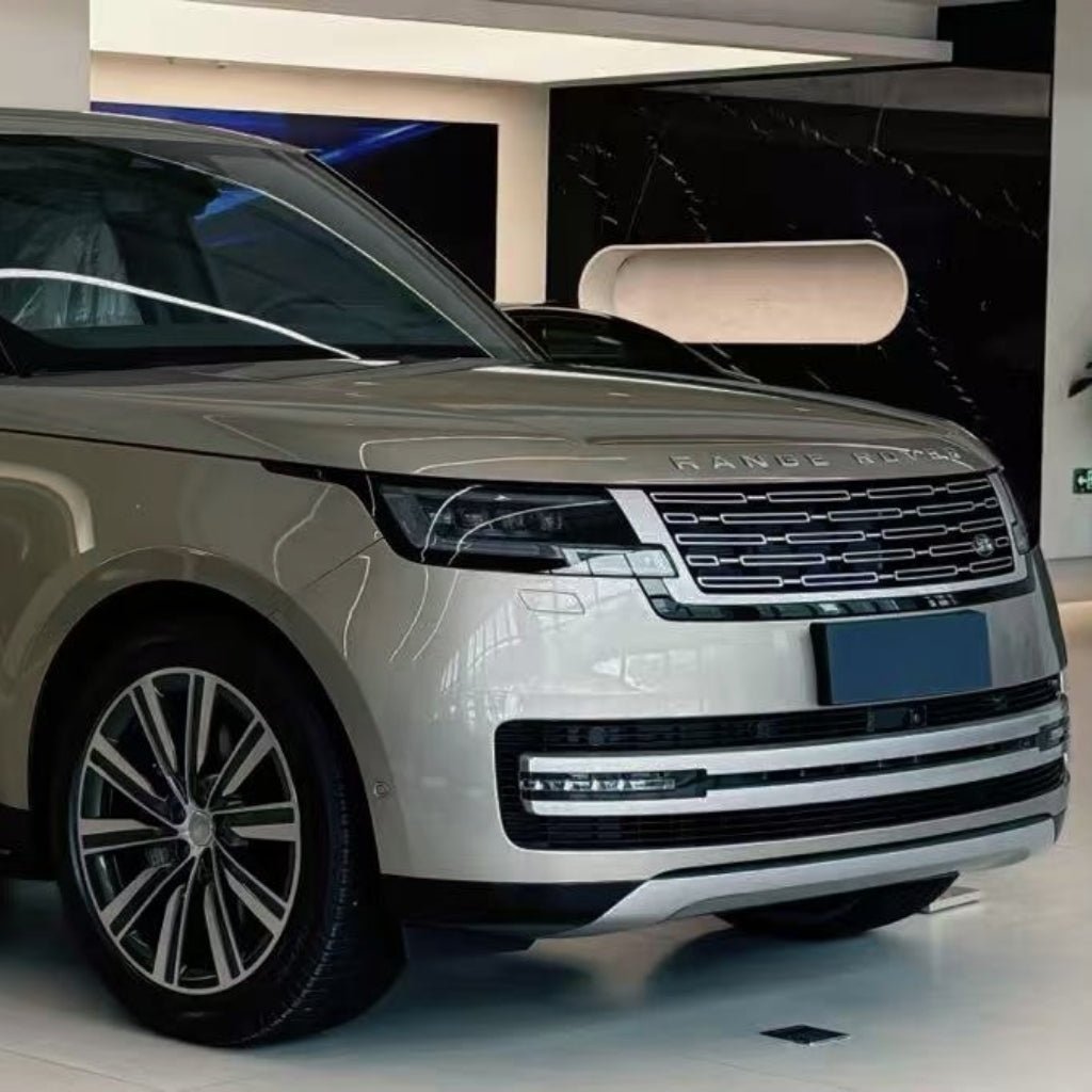 A beige Range Rover SUV is parked in a modern showroom, its front and side highlighted with Batumi Gold Liquid Metallic Glossy SelfRepair Nano-Coated PPF, showcasing the distinctive grille, sleek headlights, and alloy wheels.