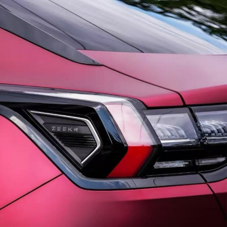 Close-up of the rear taillight on a red Zeekr car, protected by Diamond Brilliant Magenta Glossy SelfRepair Nano-Coated PPF, showcasing the brand logo and sleek design with greenery softly blurred in the background.