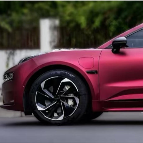 A close-up shows the front of a shiny red car with Diamond Brilliant Magenta Glossy SelfRepair Nano-Coated PPF, highlighting the wheel, side mirror, and headlight against a blurred background of greenery and a white wall.