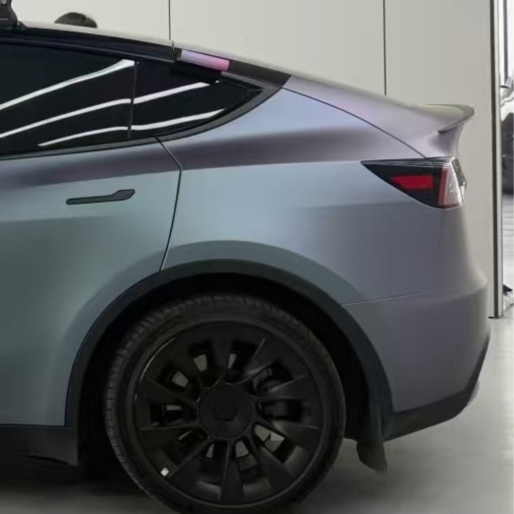Matte grey electric SUV with black wheels, seen from the side and rear, parked indoors near a white wall. Modern curves and lines are protected by Capri Gray Purple Matte SelfRepair Nano-Coated PPF for added durability.