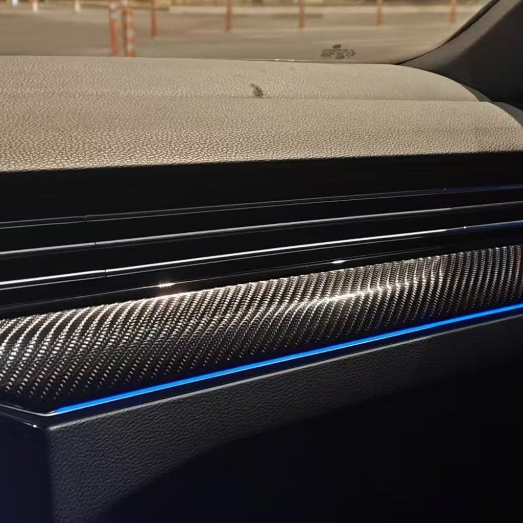 Close-up of a car dashboard featuring Carbon Fiber Carbon SelfRepair Nano-Coated PPF trim, textured surface, black air vent, and thin blue LED accent light, with a parking lot and orange cones visible through the windshield.
