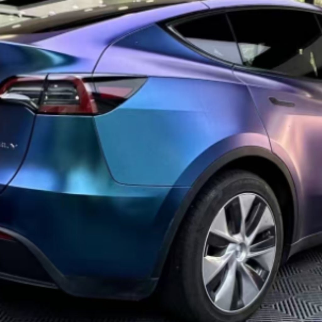A close-up of the rear side of a Tesla Model Y features a Chameleon Purple Blue Green Matte SelfRepair Nano-Coated PPF wrap, parked on a patterned surface.