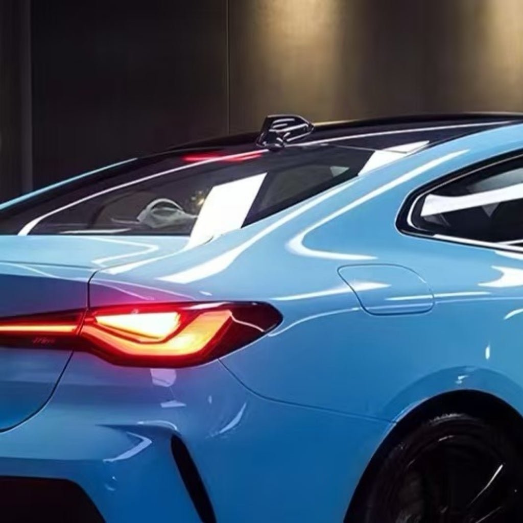Close-up of the rear of a bright blue sports car with sleek lines, red taillight, and black roof, surface protected by Sky Blue Charm SelfRepair Nano-Coated PPF, inside a modern, well-lit garage or showroom.
