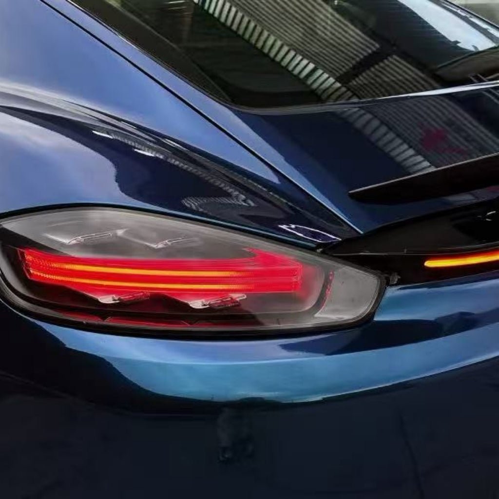 Close-up of the rear left taillight of a sleek sports car in Diamond Dark Shadow Blue Glossy SelfRepair Nano-Coated PPF, reflecting roof and windows. The lit taillight shows red horizontal lines with an orange indicator strip above.