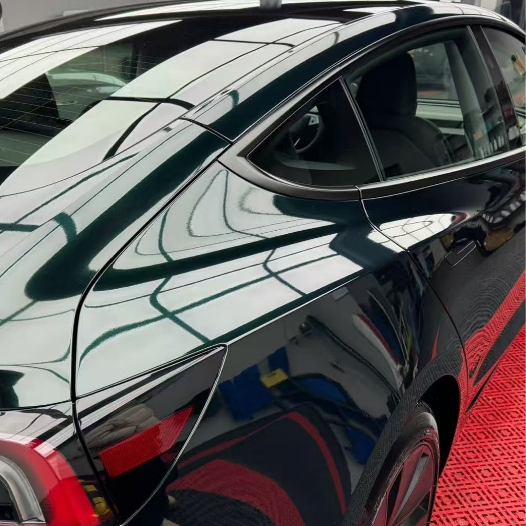 A close-up of a shiny black car indoors shows its Diamond Emerald Glossy SelfRepair Nano-Coated PPF reflecting ceiling lights, with a red and black patterned floor below for enhanced automotive protection.