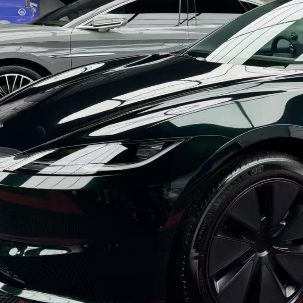 Two modern cars are parked side by side indoors, with the sleek front and side of a black car in the foreground featuring Diamond Emerald Glossy SelfRepair Nano-Coated PPF, while a grey car is partially visible in the background.