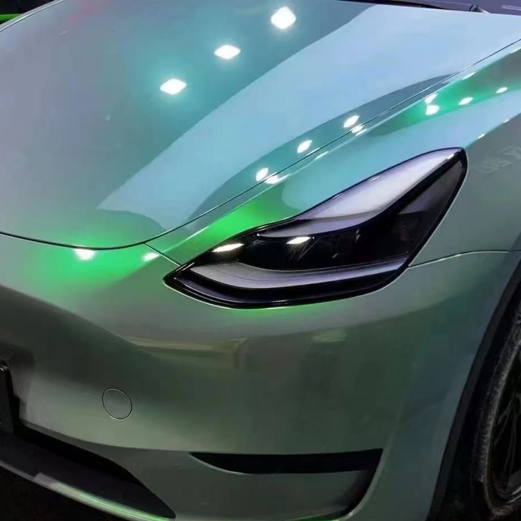 Close-up of the front left side of a metallic silver car with Gray to Green Charm Glossy SelfRepair Nano-Coated PPF for ochrana karosérie. Headlight and hood shine with reflected lights, enhanced by self-repairing nano technology.