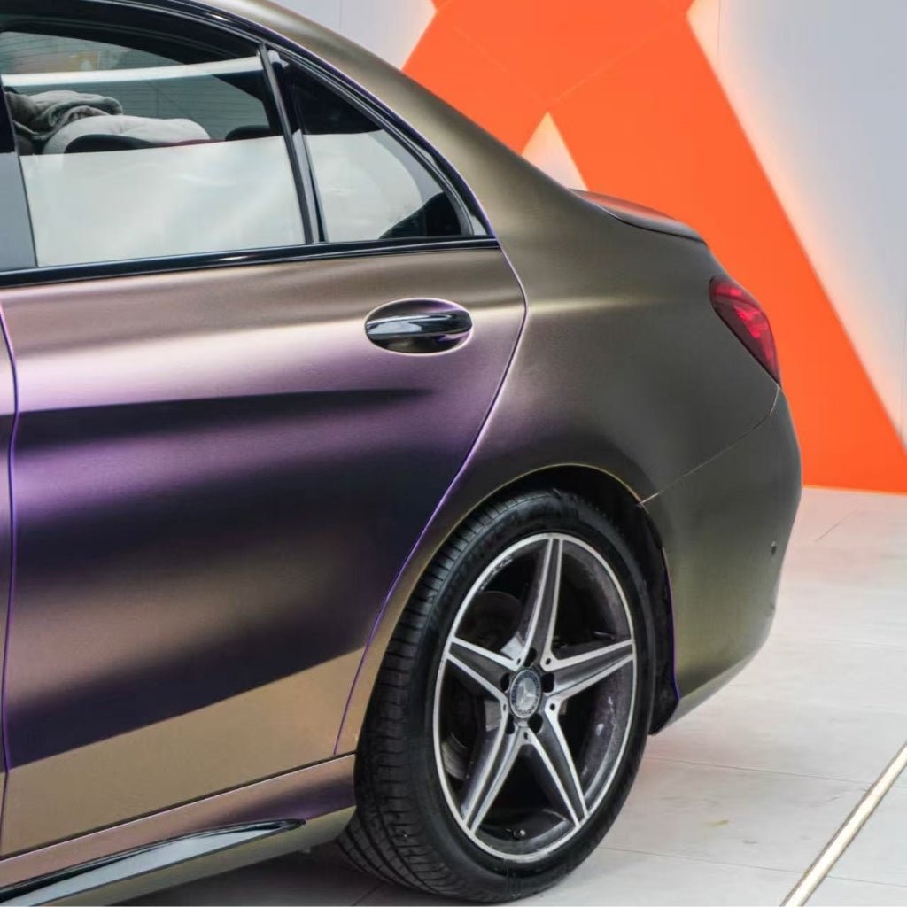 A close-up of a car’s rear with Gold Red Purple Chameleon SelfRepair Nano-Coated PPF, five-spoke alloy wheel, and gradient paint for a unique color effect. The background shows an orange geometric wall design.