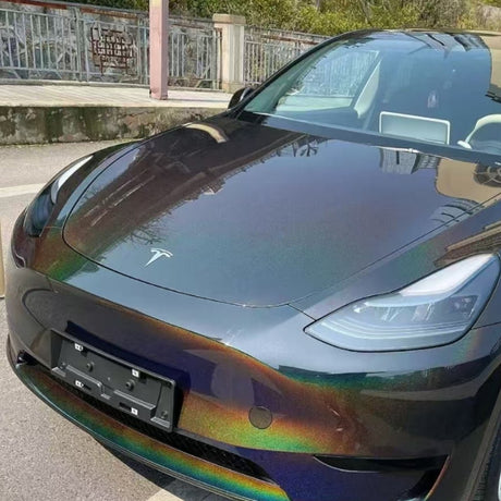 A Tesla with a striking Black Galaxy Glossy SelfRepair Nano-Coated PPF paint job is parked on a street near a metal fence and stone sidewalk.