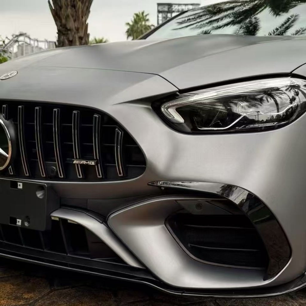 Close-up of the front end of a silver Mercedes-AMG with AMG badge, headlight, and bumper. Palm tree reflections appear on the hood, protected by AMG Mountain Gray Matte SelfRepair Nano-Coated PPF.