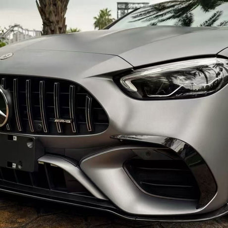 Close-up of the front end of a silver Mercedes-AMG with AMG badge, headlight, and bumper. Palm tree reflections appear on the hood, protected by AMG Mountain Gray Matte SelfRepair Nano-Coated PPF.