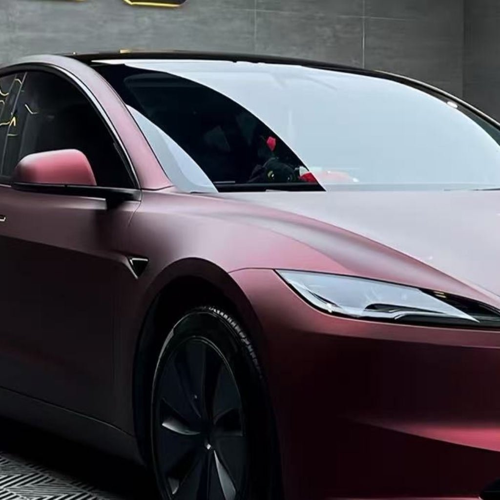 A modern electric car, wrapped in Dragon Blood Red Matte SelfRepair Nano-Coated PPF, features aerodynamic curves, tinted windows, and black wheels. The matte film enhances its style in a chic showroom or garage with gray walls.