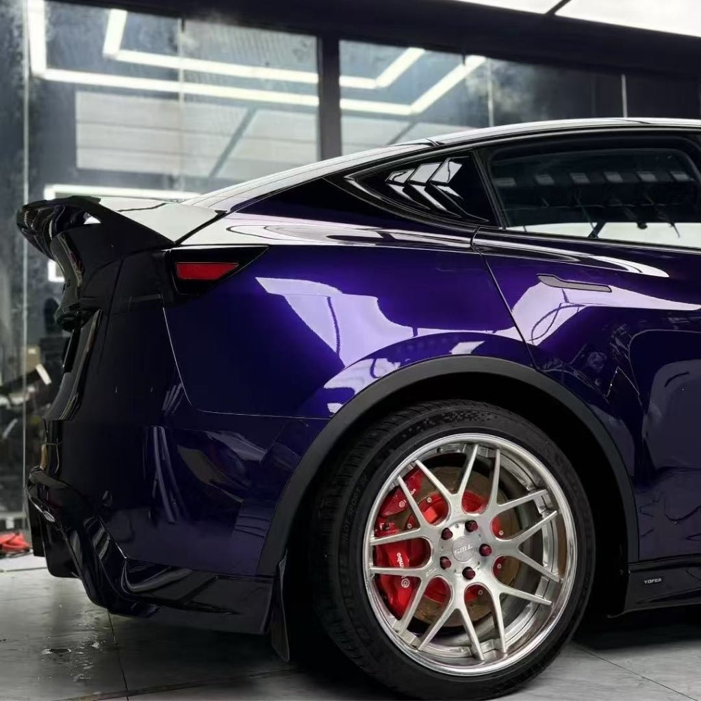 A close-up side view of a dark purple car in a garage highlights its rear spoiler, shiny alloy wheels, and red brake calipers under bright lights—with Diamond Midnight Purple Glossy SelfRepair Nano-Coated PPF for exceptional paint protection.