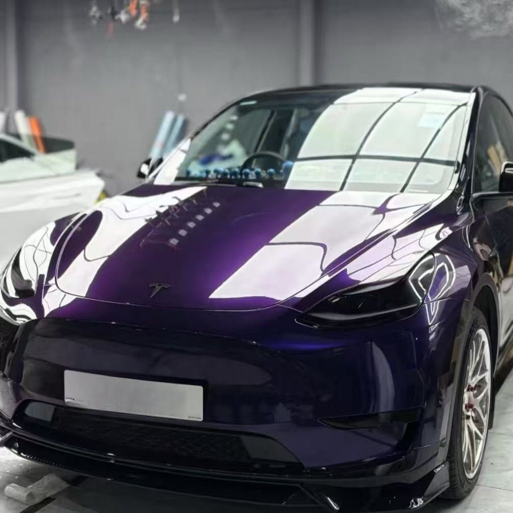 A shiny purple Tesla, wrapped in Diamond Midnight Purple Glossy SelfRepair Nano-Coated PPF, is parked indoors under bright lights, reflecting the ceiling and surroundings on its hood and windshield for maximálna ochrana laku auta.