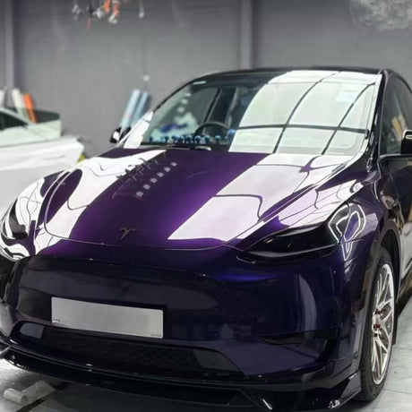 A shiny purple Tesla, wrapped in Diamond Midnight Purple Glossy SelfRepair Nano-Coated PPF, is parked indoors under bright lights, reflecting the ceiling and surroundings on its hood and windshield for maximálna ochrana laku auta.