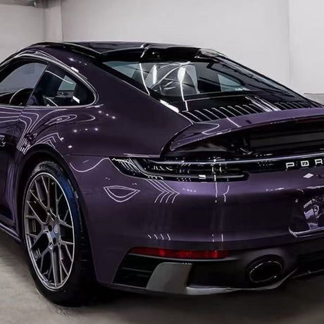 A sleek purple Porsche sports car, protected by Diamond Provence Purple Glossy SelfRepair Nano-Coated PPF, is parked indoors. Its glossy finish, striking taillights, and large alloy wheels gleam under bright showroom lights.