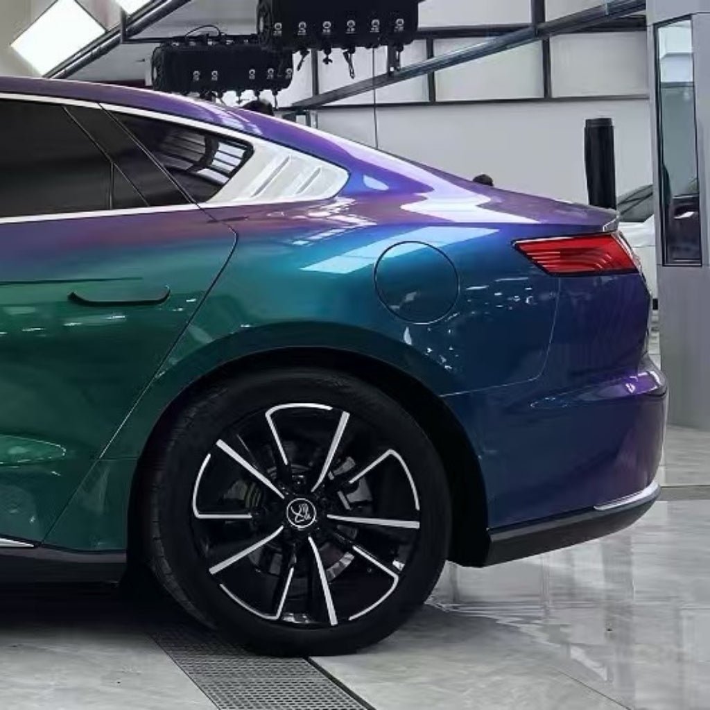 The image displays the rear of a shiny sedan wrapped in Red Blue Green Chameleon SelfRepair Nano-Coated PPF, reflecting vibrant blue, green, and purple hues. The car is indoors on a glossy floor near a large window.
