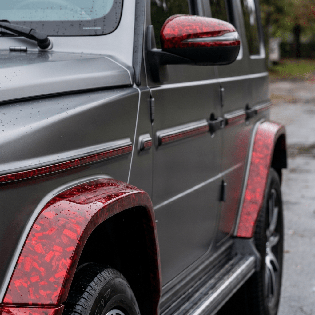 A matte gray SUV features Red Forged Carbon Graphite Self-Healing Nano-Coated PPF on its fender, mirror, and trim. Water droplets bead on the surface as blurred greenery appears in the background.