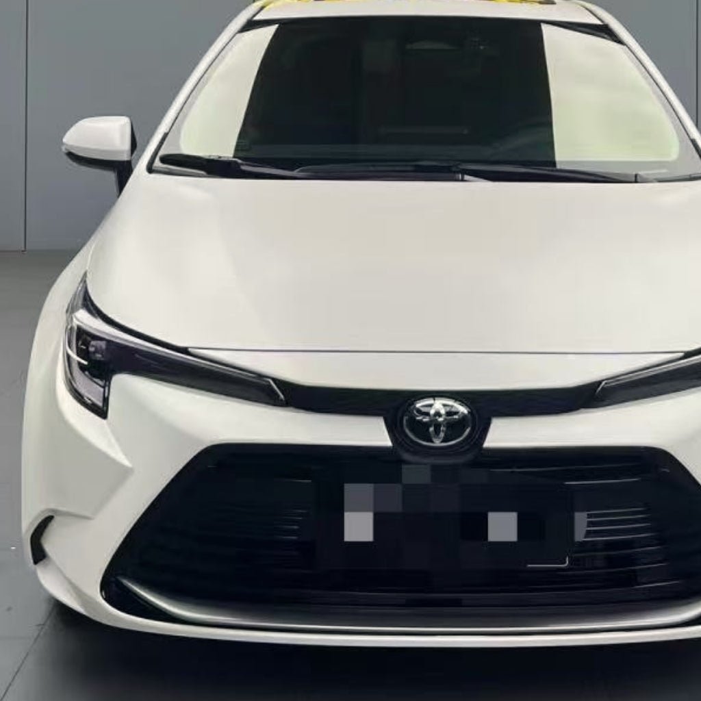 Front view of a white Toyota sedan indoors, showcasing its grille, headlights, and Toyota emblem. The car is protected with Satin Liquid Metallic Bronze SelfRepair Nano-Coated PPF. Neutral gray background.