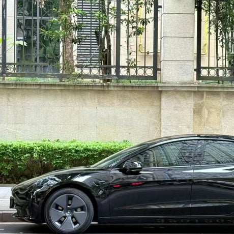A sleek car protected by Shell Black Glossy SelfRepair Nano-Coated PPF is parked beside a stone wall with iron railings and greenery, showcasing its glossy finish on the front half—door, mirror, and wheel—in the photo.