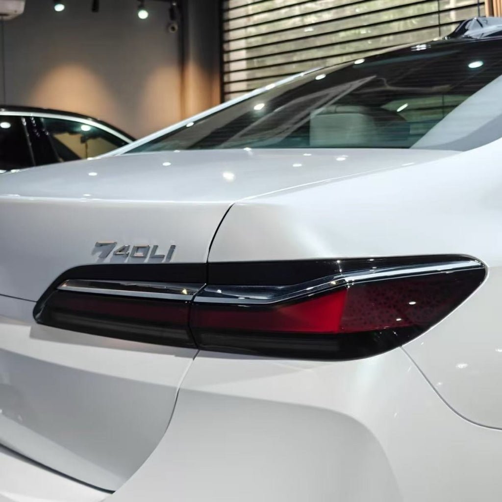Rear view of a white BMW 740Li sedan in a modern showroom, featuring sleek tail lights and model badge. The car is protected with Shell White Glossy SelfRepair Nano-Coated PPF for lasting shine and durability, with reflections and window blinds in the scene.