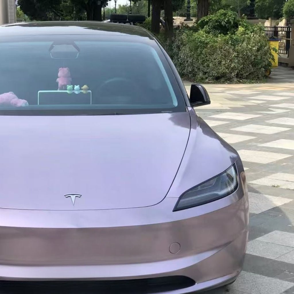 A pink Tesla with Sunshine Purple Liquid Metallic Matte SelfRepair Nano-Coated PPF is parked on patterned pavement by green bushes. Plush toys on the dashboard highlight the car's style and protection with this metalická fólia na auto.