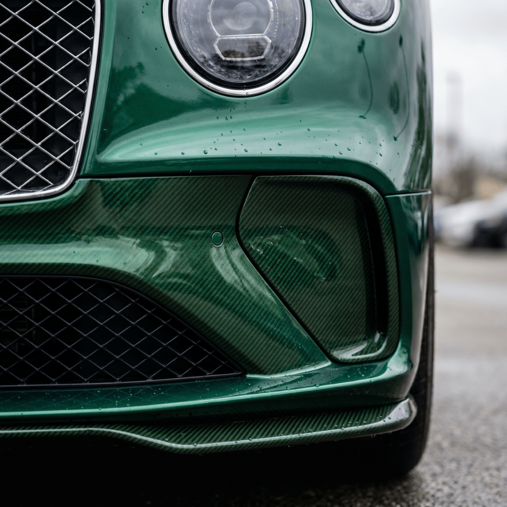 Close-up of a green luxury sports car's front corner, featuring its headlight, grille, and bumper with water droplets on Transparent Carbon Fiber Self-Healing Nano-Coated PPF for advanced surface protection.