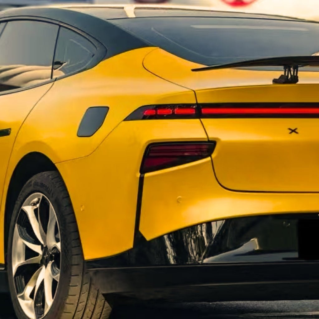 A close-up of the rear and side of a yellow electric car wrapped in Racing Yellow Glossy SelfRepair Nano-Coated PPF, showcasing sleek lines, a continuous red tail light, black trim accents, and modern alloy wheels.