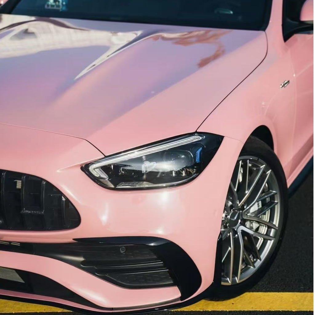 Close-up of the front left side of a shiny Rouge Pink Glossy SelfRepair Nano-Coated PPF car, with a modern headlight and silver alloy wheel, serving as an ochranná bariéra vozidla, parked beside a yellow road line.