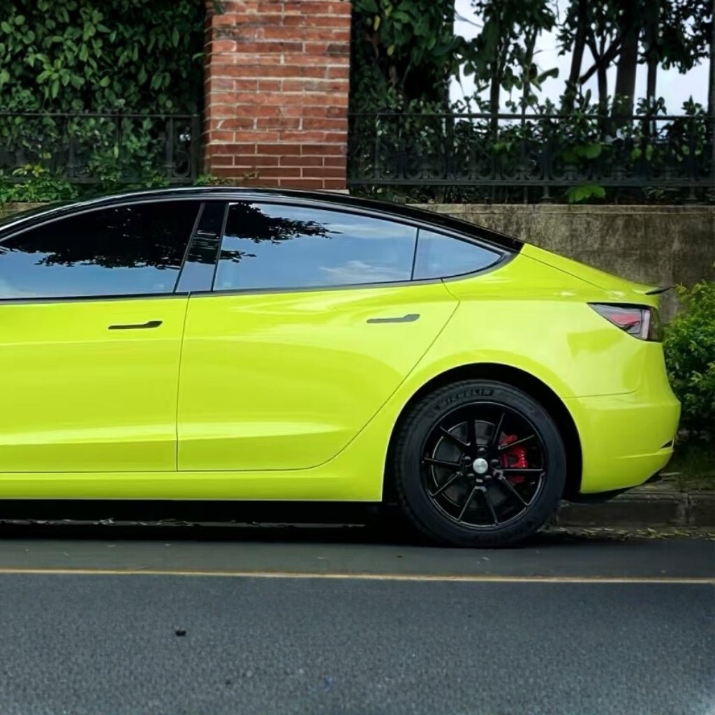 A bright yellow electric car with black wheels, protected by São Paulo Glossy SelfRepair Nano-Coated PPF, is parked beside a brick pillar and stone wall, with greenery and trees in the background.