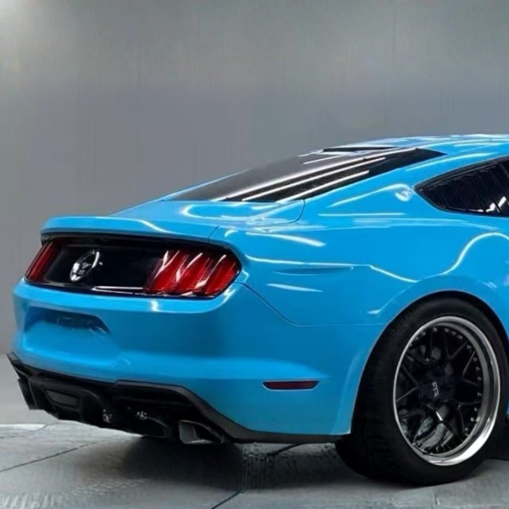 A bright blue sports car with Sky Blue Glossy SelfRepair Nano-Coated PPF, black wheels, red taillights, a black rear spoiler, and a sleek design is shown from the rear side angle against a plain gray background.