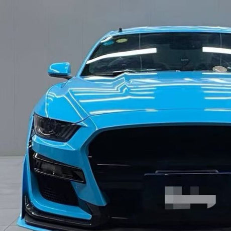 A vibrant blue sports car, viewed from the front indoors, showcases sharp headlights and a large black grille. It's protected with Sky Blue Glossy SelfRepair Nano-Coated PPF for a brilliant finish and superior scratch resistance.