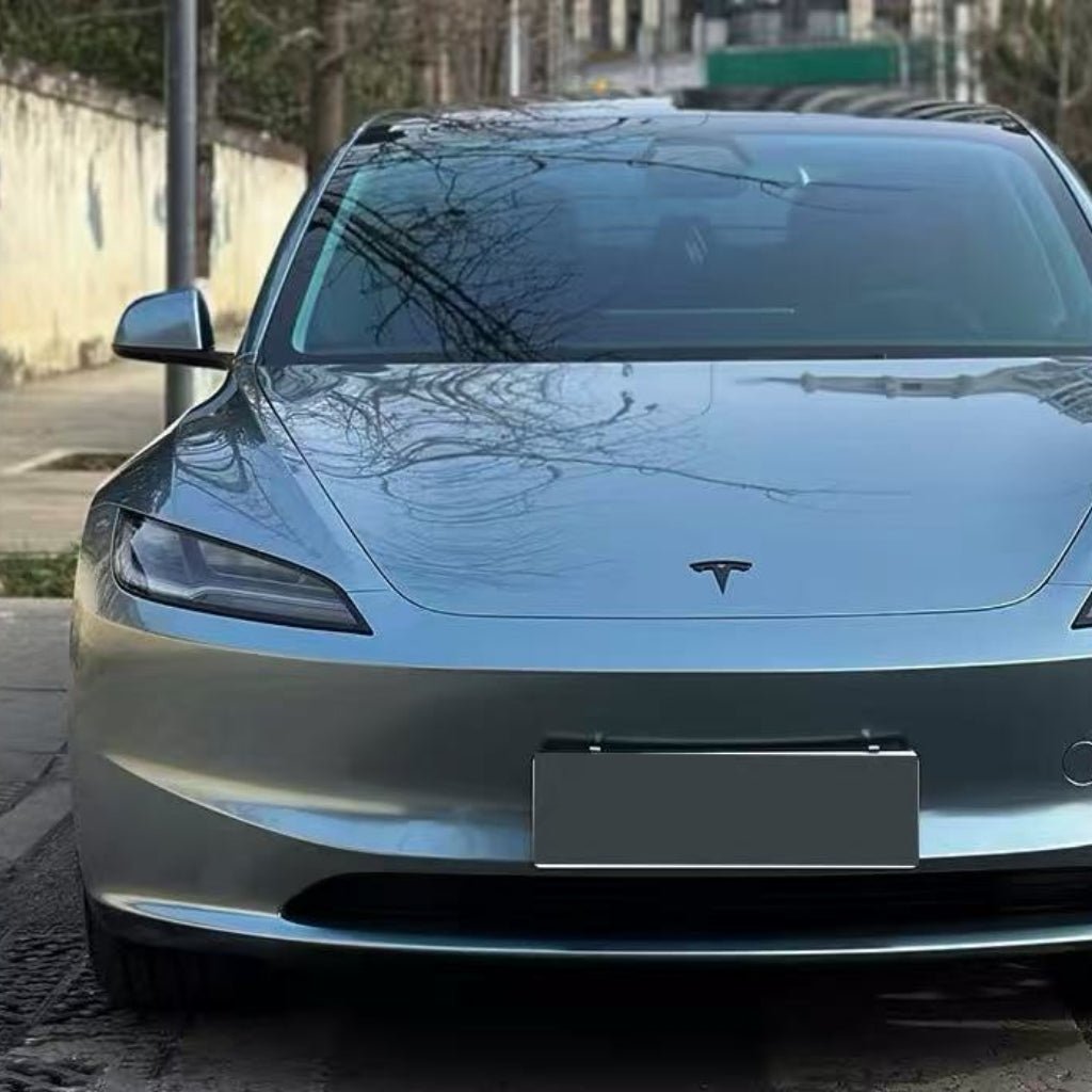 A silver Tesla Model 3 with a sleek design and distinctive logo is parked on the street, shielded by Polar Titanium Liquid Metallic Glossy SelfRepair Nano-Coated PPF for premium ochranná fólia na auto. Trees and buildings reflect on its windshield.