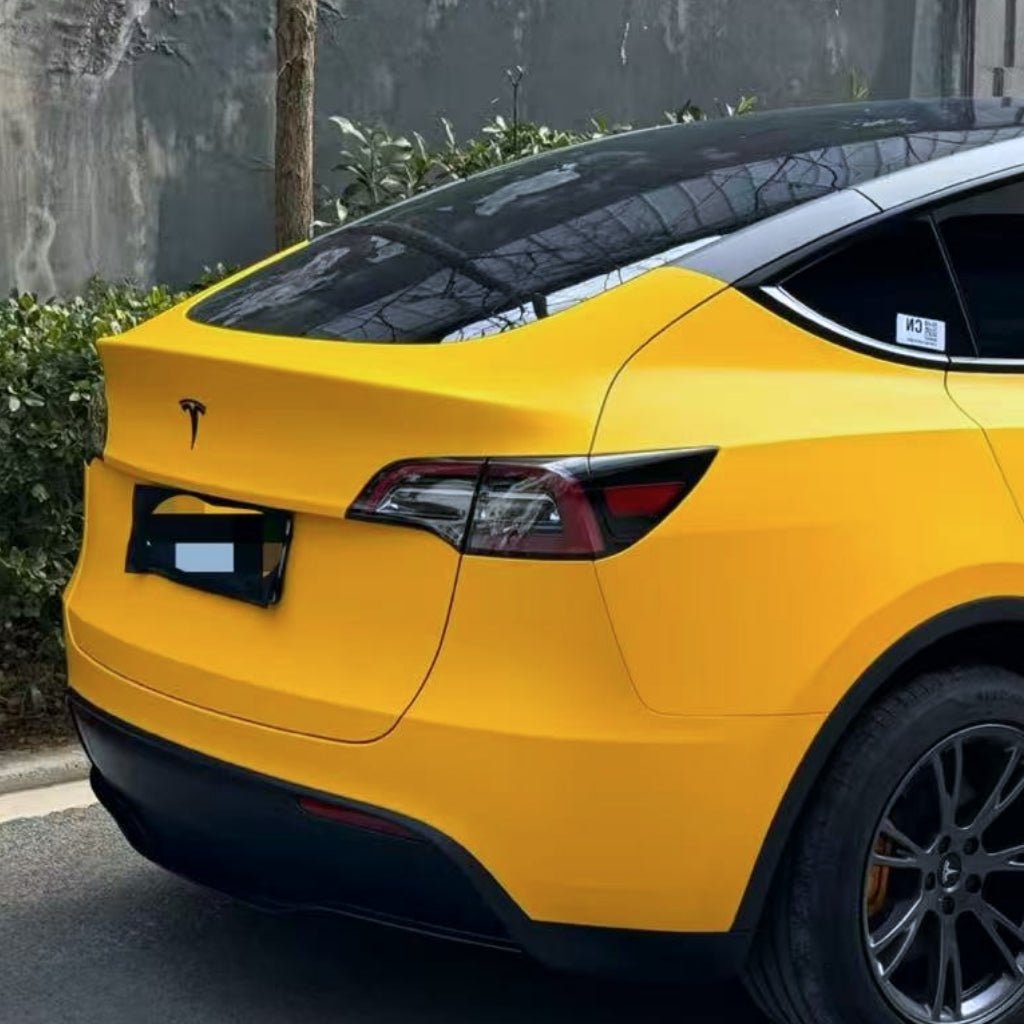 A yellow Tesla with tinted windows, protected by Sunshine Yellow Glossy SelfRepair Nano-Coated PPF, is parked on the street near green bushes and a gray wall. The image highlights the car's rear and side.