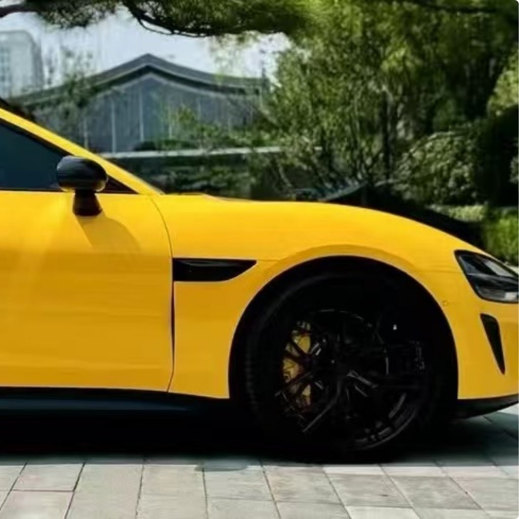 A bright yellow sports car, protected by Sunshine Yellow Glossy SelfRepair Nano-Coated PPF, is parked on a paved area, with lush green trees and a modern building providing a vibrant backdrop.