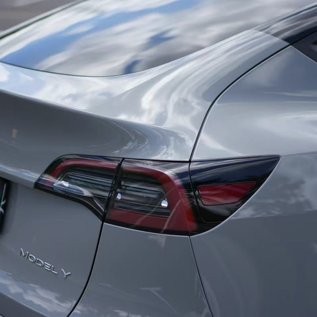 Close-up of the rear of a silver Tesla Model Y with Volcano Gray Glossy SelfRepair Nano-Coated PPF, highlighting the taillight and curves as sky and clouds reflect beautifully on the ochranný film na lak surface.