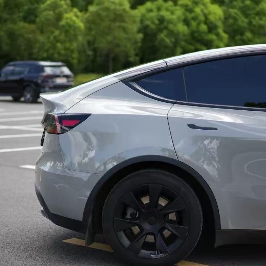 A silver car, partially shown from the side and protected with Volcano Gray Glossy SelfRepair Nano-Coated PPF, is parked in a sunny parking lot with surrounding trees. In the background, a black car adds to the scene's calm atmosphere.