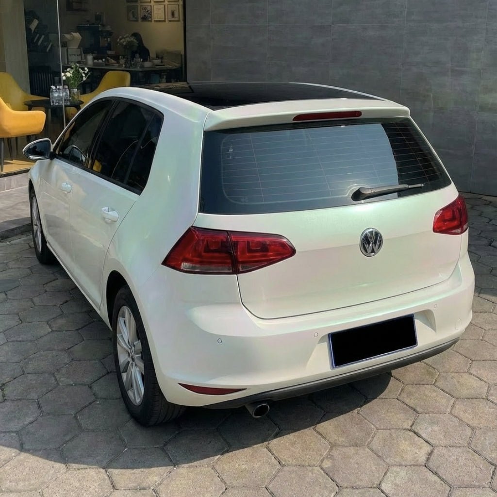 A white Volkswagen hatchback with White Diamond Green Glossy SelfRepair Nano-Coated PPF is parked on a stone-paved driveway near a building with large windows and a yellow chair visible inside.